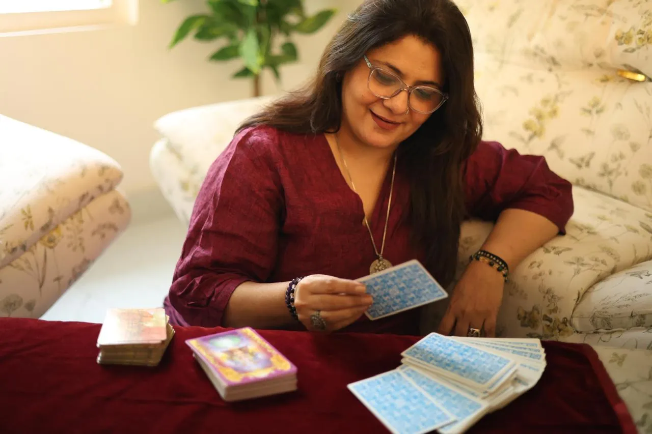 Sapnaa Khemani reading tarot at a maroon cloth table, drawing a card with two decks beside her
