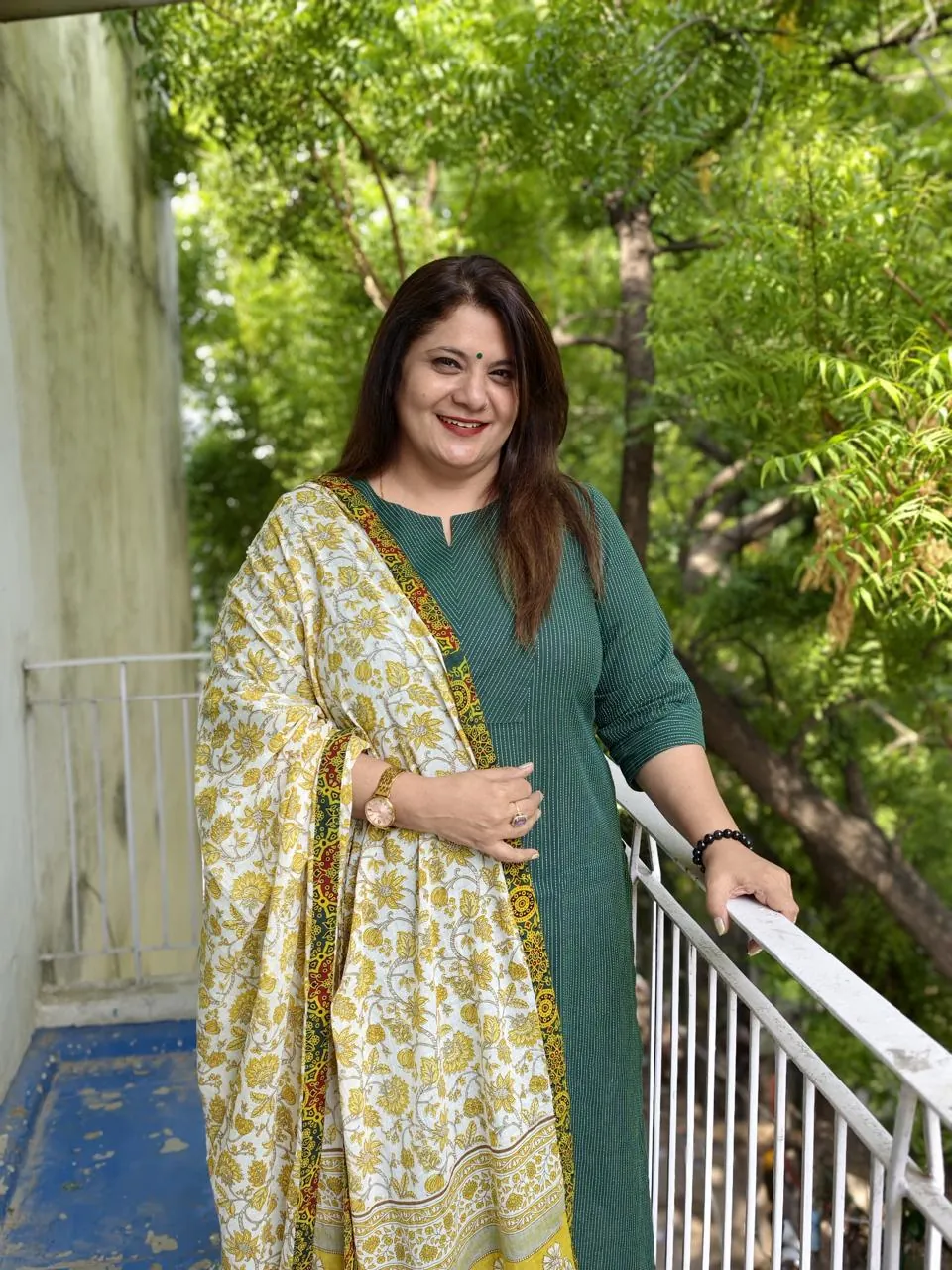 Sapnaa Khemani standing at a balcony railing in a green kurta and printed dupatta