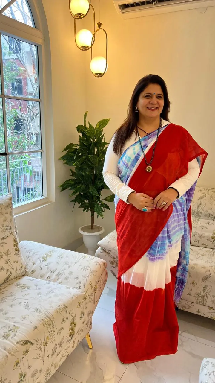 Sapnaa Khemani standing in a red and blue tie-dye saree in a sunlit sitting room