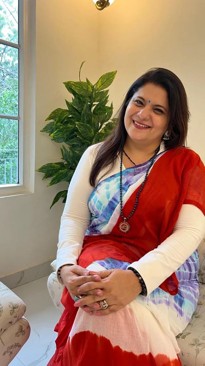 Sapnaa Khemani seated in a tie-dye saree, smiling towards the camera
